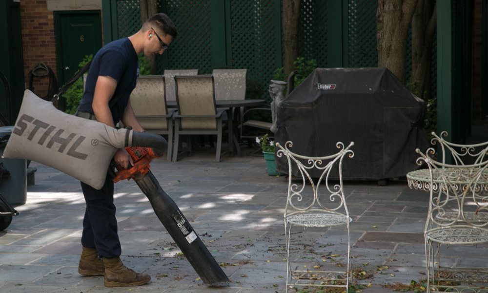 A workman using a leaf vacuum on a patio area