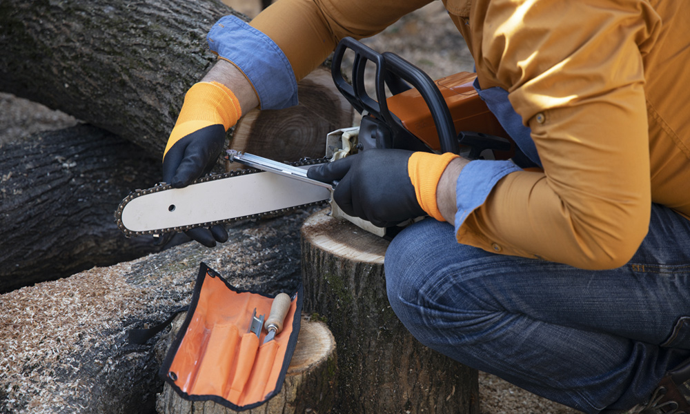 A man using his chainsaw sharpener kit to sharpener his chainsaw chain