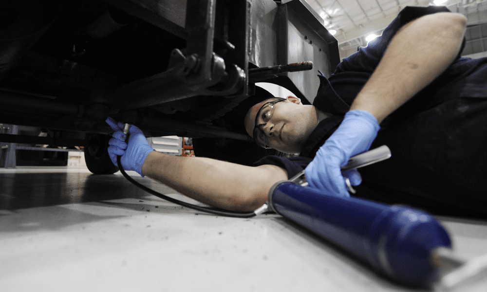 A man laying down on the floor using a grease gun