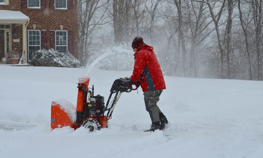 A man using a snow blower to clear his driveway