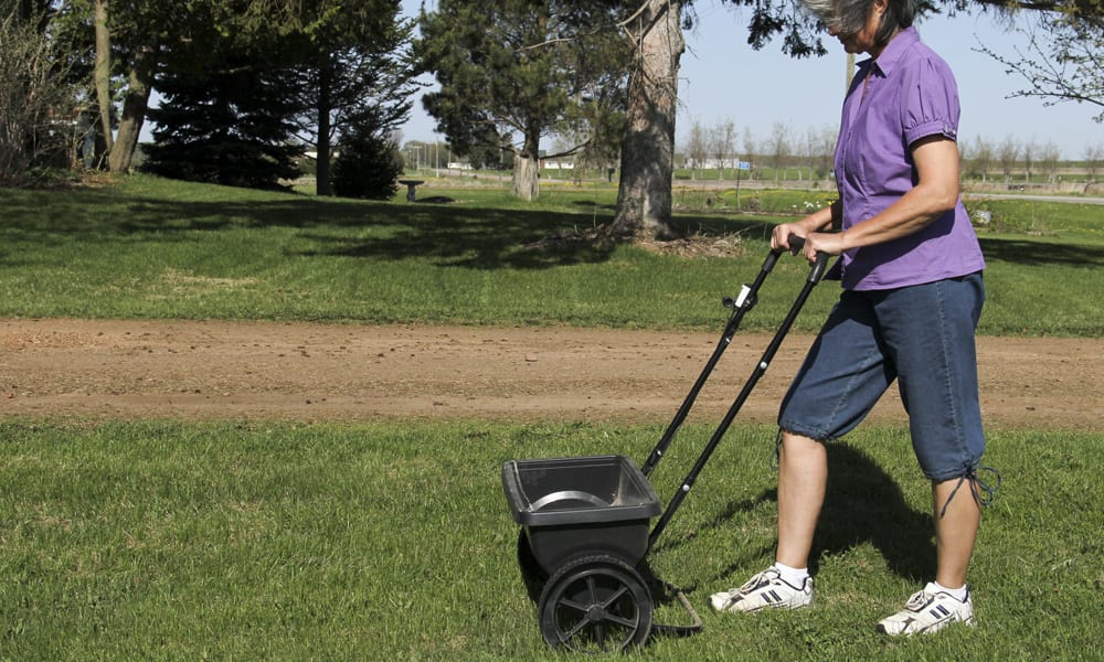 A woman pushing a Spreader over grass
