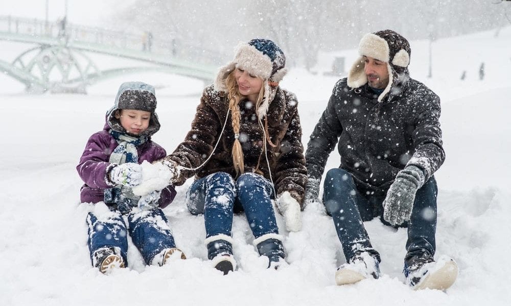 a family sitting in snow while its snowing.