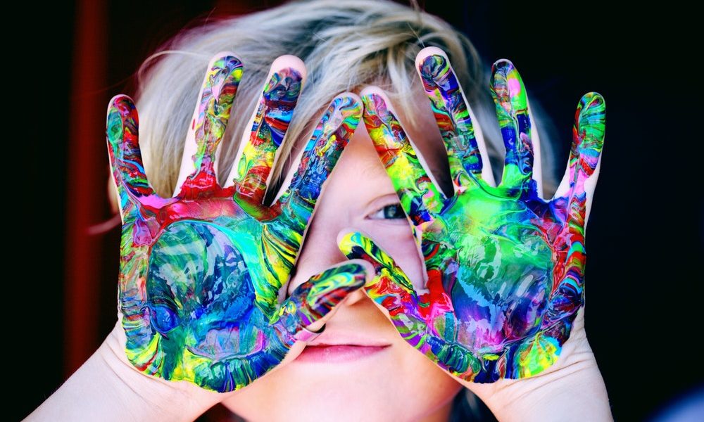 child hands covered in different color paints