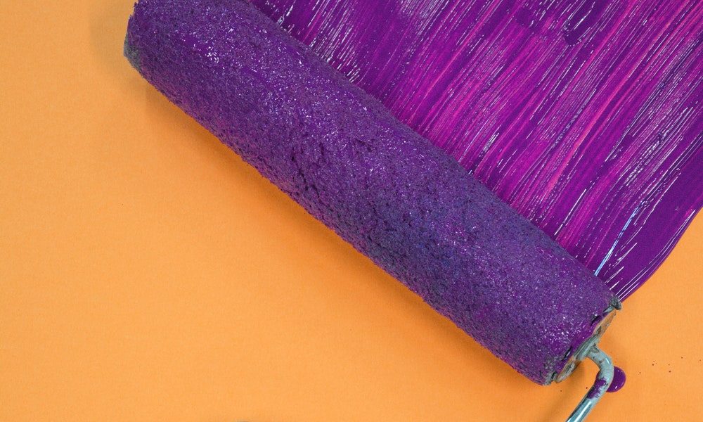 purple paint roller painting over orange wall
