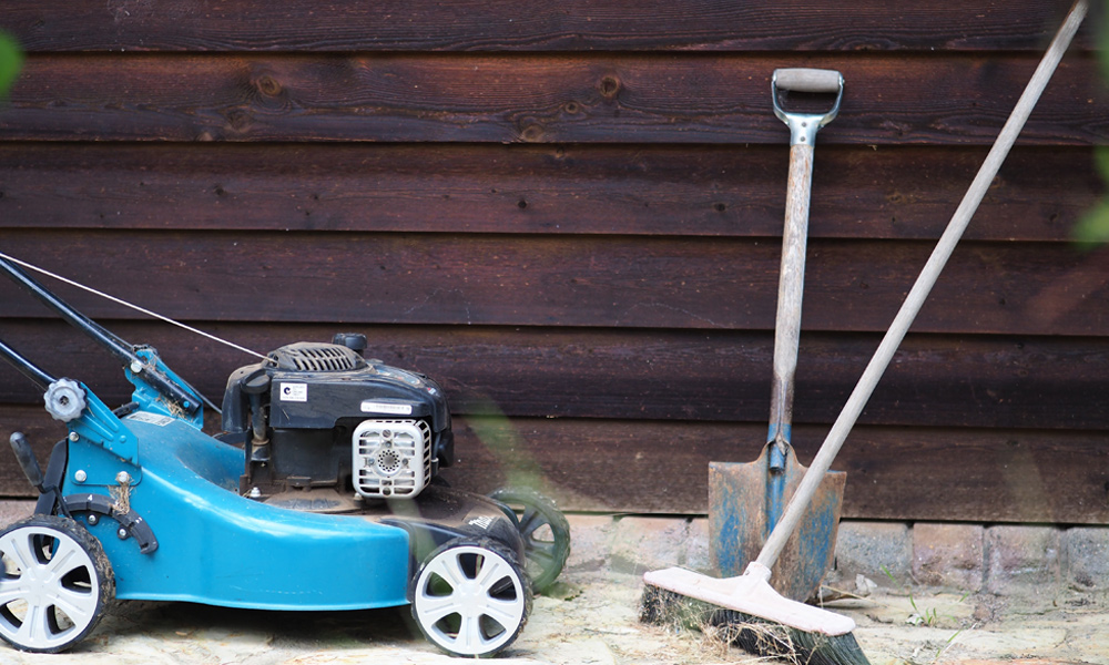 gas lawn mower with broom and spade next to it.